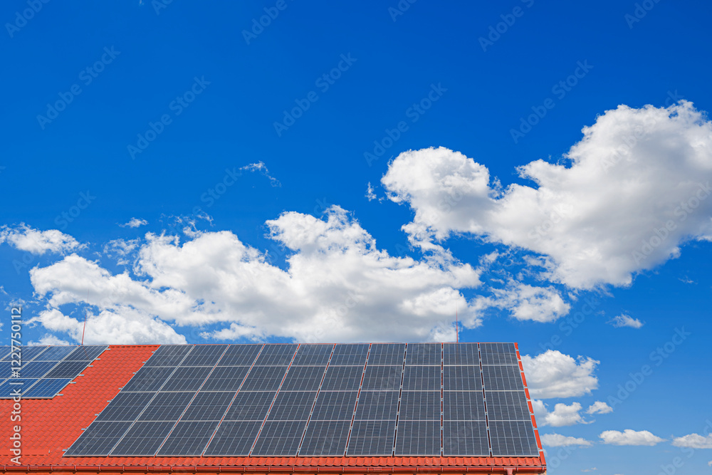 A set of solar panels is installed on the roof of a building with red tiles under a clear blue sky.