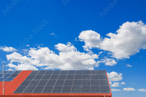Obraz na płótnie A set of solar panels is installed on the roof of a building with red tiles under a clear blue sky. w salonie