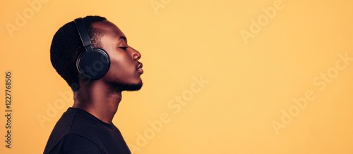 Young man with headphones in a warm-toned studio setting showcasing concentration and creative energy with ample copy space for text