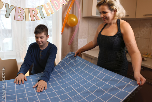 A woman with her son and nephew decorate a room and a festive table for a birthday celebration. Soft lighting.