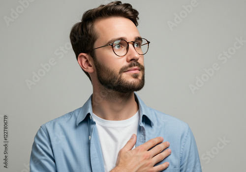 Man with glasses and beard holding hand on chest looks up. Thoughtful man with emotional expression and hand on chest