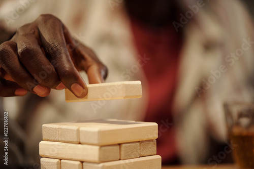 Hand of young African American man putting wooden block on top of tower while playing leisure game photo