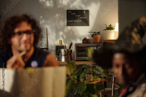 Focus on poster with lifestyle slogan hanging on wall of domestic kitchen with friends playing board game photo