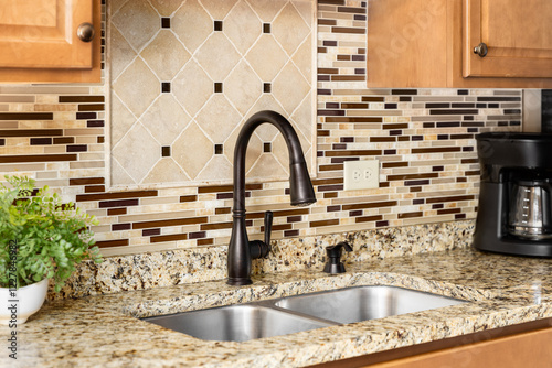 A kitchen faucet detail with wood cabinets, an oil rubbed bronze faucet, quartz countertop, and glass and stone tile backsplash.