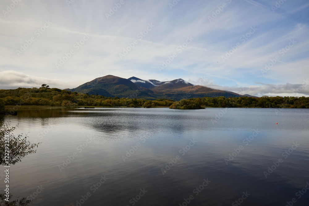 A peaceful view of Lough Leane with its calm waters reflecting the surrounding landscape and distant mountains, located near Ross Castle in County Kerry, Ireland. An idyllic natural scene. A peaceful view of Lough Leane with its calm waters reflecting the surrounding landscape and distant mountains, located near Ross Castle in County Kerry, Ireland. An idyllic natural scene.