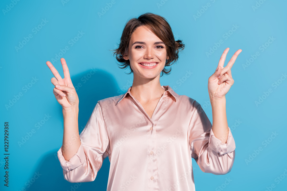 Charming young businesswoman in a satin blouse making peace signs on a blue background Charming young businesswoman in a satin blouse making peace signs on a blue background