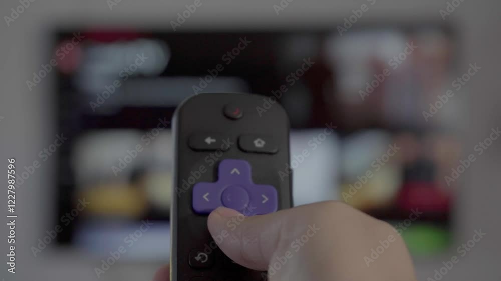 Hand holding a remote control in front of a smart TV screen, symbolizing streaming, entertainment, digital media, modern technology, apps, connectivity, and home relaxation, symbolizing entertainment.