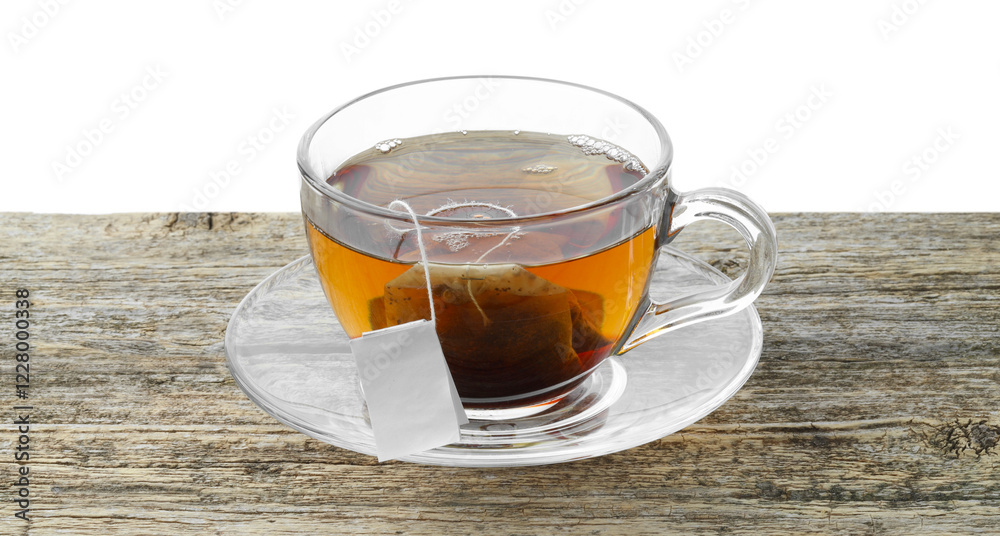 Tea bag in glass cup with hot drink on wooden table against white background Tea bag in glass cup with hot drink on wooden table against white background