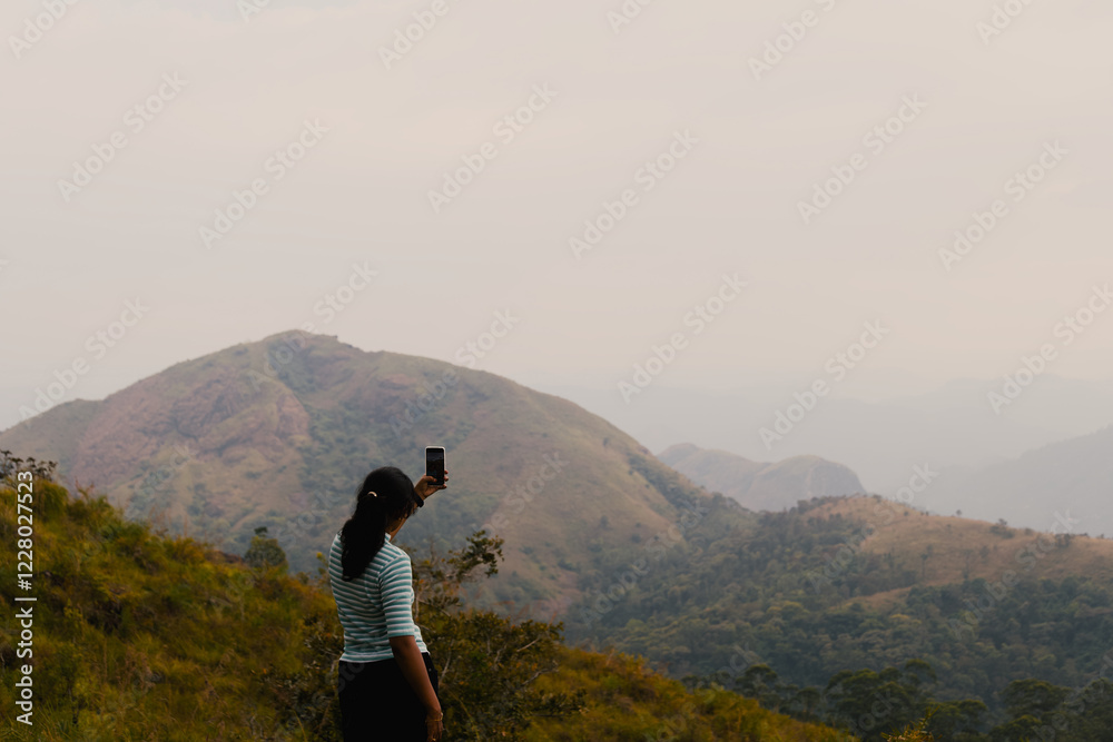 Woman taking photo with mobile phone on top of mountain in morning time Woman taking photo with mobile phone on top of mountain in morning time