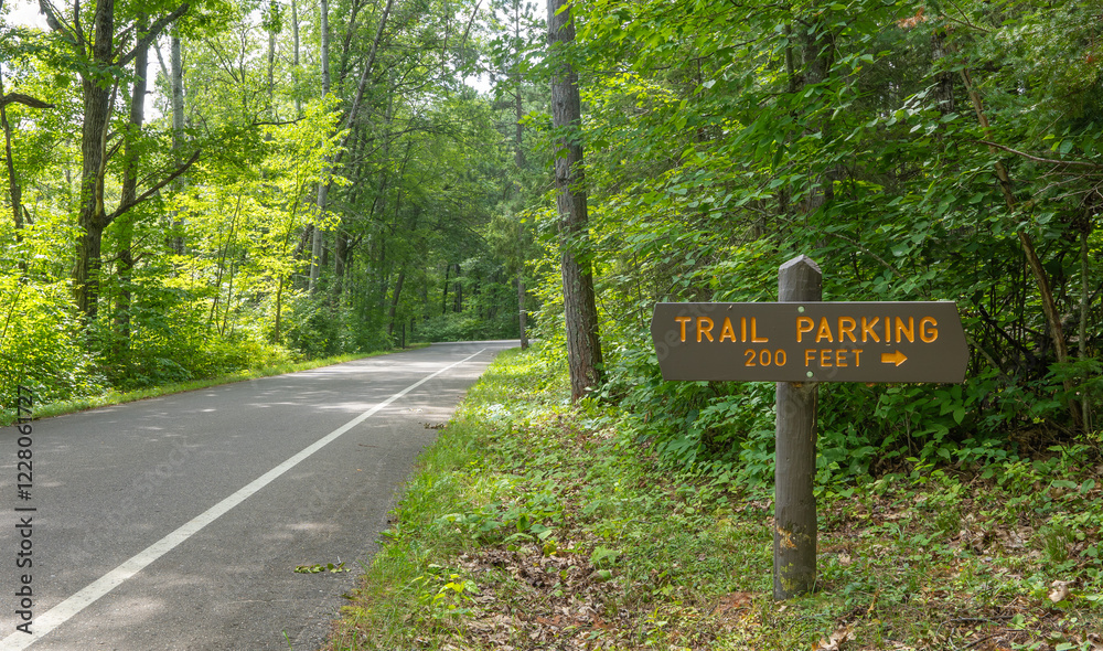 Forest asphalt road and green trees and a sign indicating Trail Parking in 200 Feet with directional arrow.