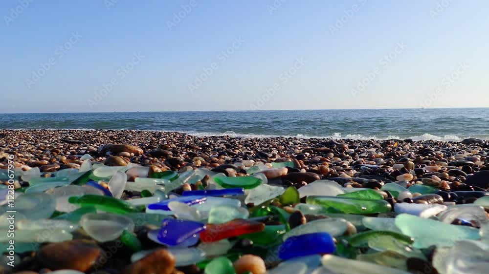 Colored sea glass with beach pebbles and shells in the mediterranean coast and in the background sea and waves with sunset and sky, sandy beach with coast glass, beach glass. Colored sea glass with beach pebbles and shells in the mediterranean coast and in the background sea and waves with sunset and sky, sandy beach with coast glass, beach glass.