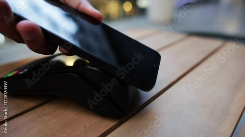 Smartphone tapping near point of sale terminal, completing wireless payment transaction on rustic wooden surface
