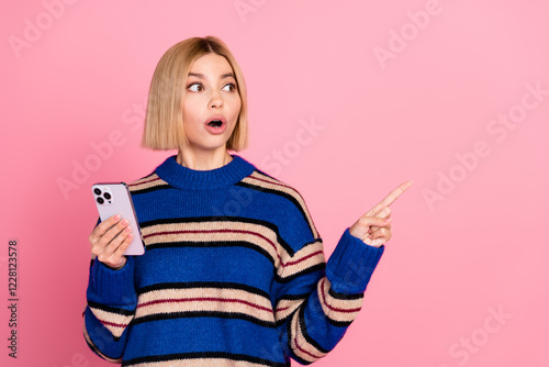 Young woman pointing aside with an impressed look holding a smartphone against a pink background photo