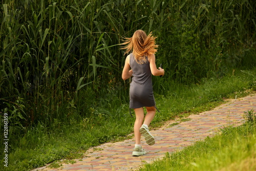 A young girl with a mobile phone in her hands in a revealing outfit with bare legs walks along a park alley among the greenery to meet her friends. Fashion of modern youth.