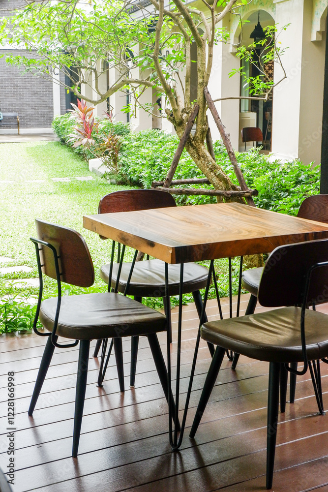 Fototapeta premium Wooden table and chair set in garden on a sunny day,outdoor seating for restaurant or cafe,Neat paved patio with sitting area and small garden in forest..