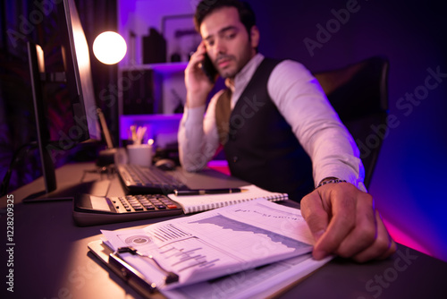 Smart businessman calling partner or investor on smartphone, discussing on target market database folder report to analyze sales channel discipline's product service at neon dark light room. Surmise. photo