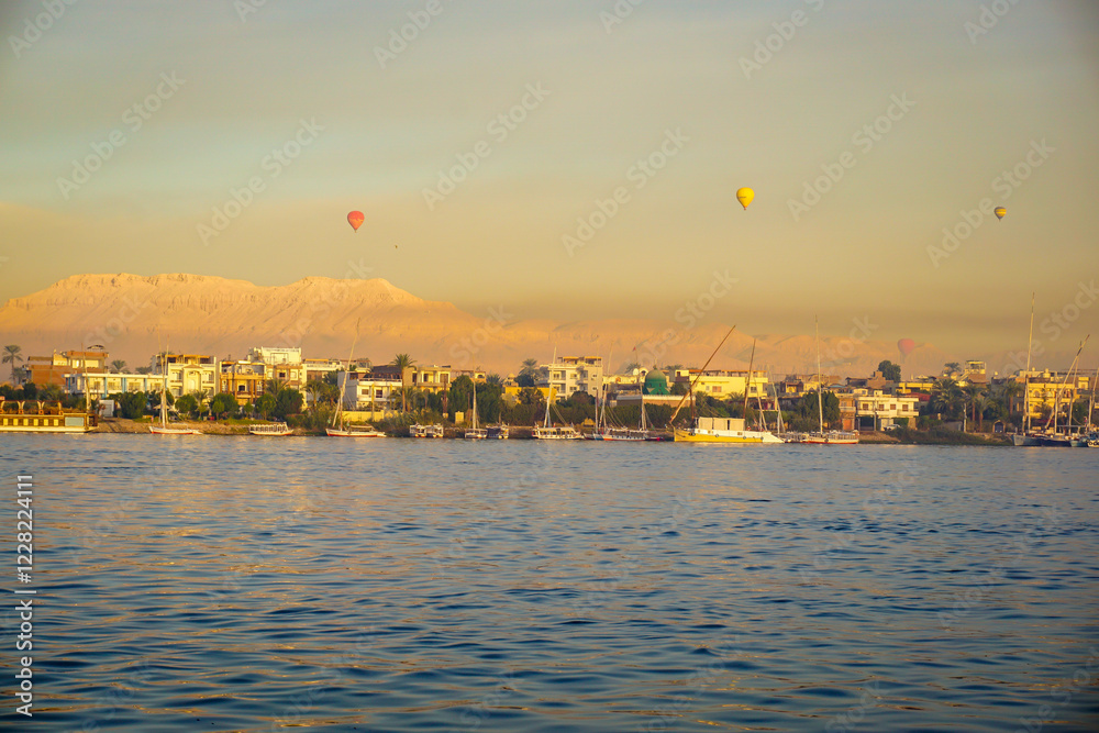 Fototapeta premium Sunrise over the Nile River in Luxor Egypt with Hot Air Balloons flying above and the Valley of the Kings in the distance