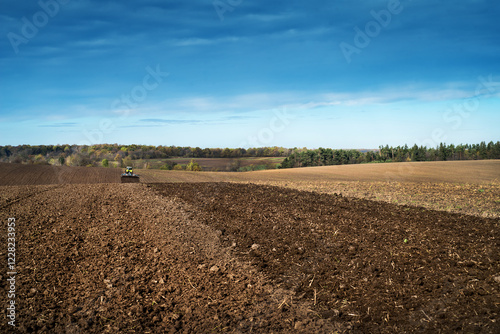Plowed farmland under a blue sky , agricultural landscape with a tractor at horison photo