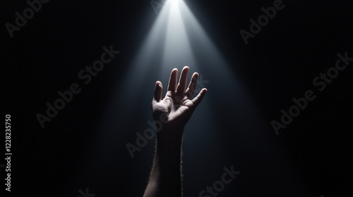 Hand reaching upwards into a spotlight in a dark room. Symbol of hope and aspiration photo