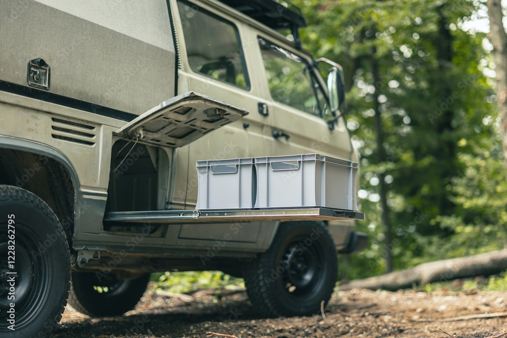 Two plastic euro box on a pull out drawer of a vintage adventure offroad vehicle or motor home, parked outside in a forest