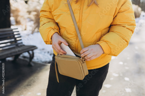 Closeup of woman's hands taking out smartphone from purse outdoors. Young stylish woman taking cellphone out of handbag. Crop anonymous female putting modern cellphone into fashionable handbag photo