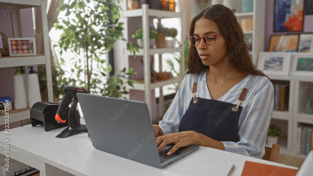 Woman working on a laptop in a home decor store with plants and shelves in the background Woman working on a laptop in a home decor store with plants and shelves in the background