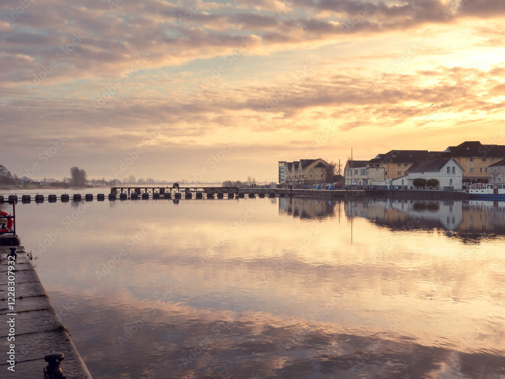 Obraz premium Athlone city riverside at warm sunset. Cloudy sky reflects in river Shannon. Popular old town, shopping, educational and industrial center. Tourist and travel hub.