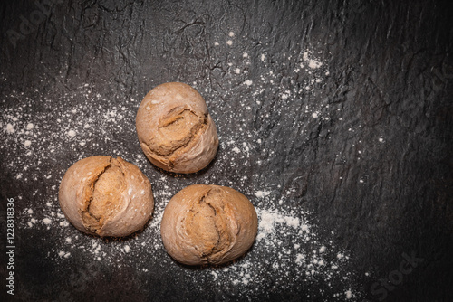 Tableau sur toile Frisch gebackene Sauerteigbrötchen auf dunkler Schieferplatte mit Mehl
