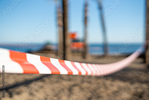 Red and White Safety Tape Blocking Access to a Beach with Palm Trees and Ocean in the Background.. photo