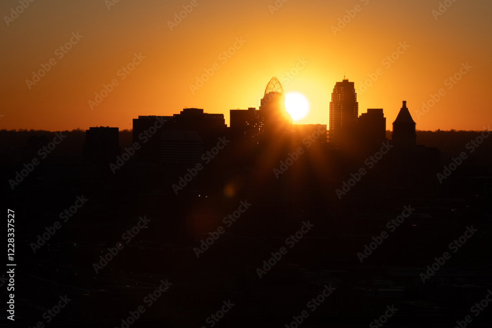 Obraz premium Sunrise over Cincinnati downtown city skyline with silhouettes of buildings and warm orange hues