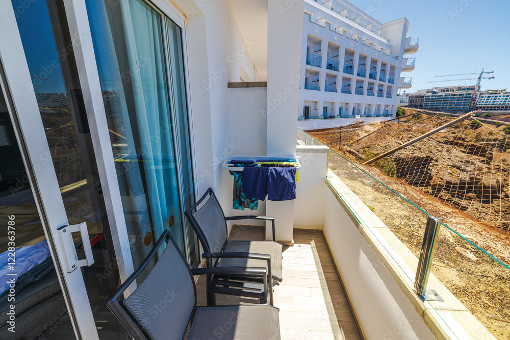 Fototapeta premium Hotel balcony on mountain top in Gran Canaria with stone railing, drying clothes, black chairs and safety net overlooking Atlantic Ocean. 