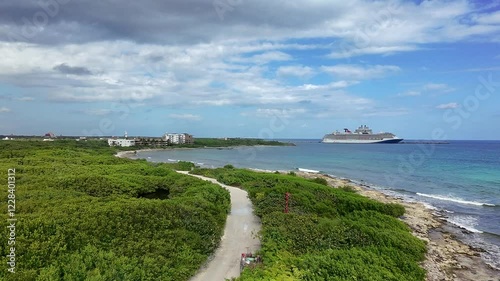 Aerial view of the coast of Mahahual Mexico shoreline and cruise port with cruise ship docked at the port surrounded by trees and vegetation with a road leading to the port. 