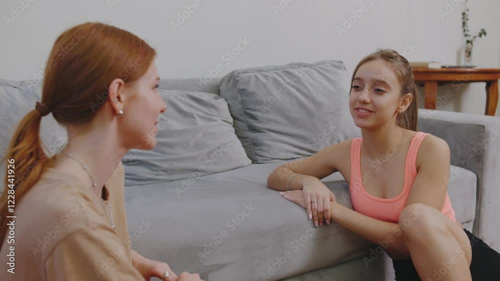 Engaging conversation between two young women in a cozy living room on the floor next to the sofa during a relaxed afternoon Engaging conversation between two young women in a cozy living room on the floor next to the sofa during a relaxed afternoon