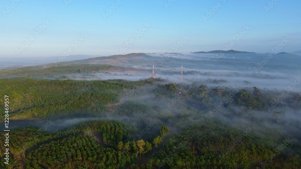 Drone view of hills with forests and trees with morning mist above with a mountainous background in the morning Drone view of hills with forests and trees with morning mist above with a mountainous background in the morning