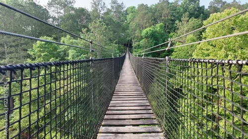 walking on a wooden and net suspension bridge through the forest over fast moving water with lush green trees and vegetation