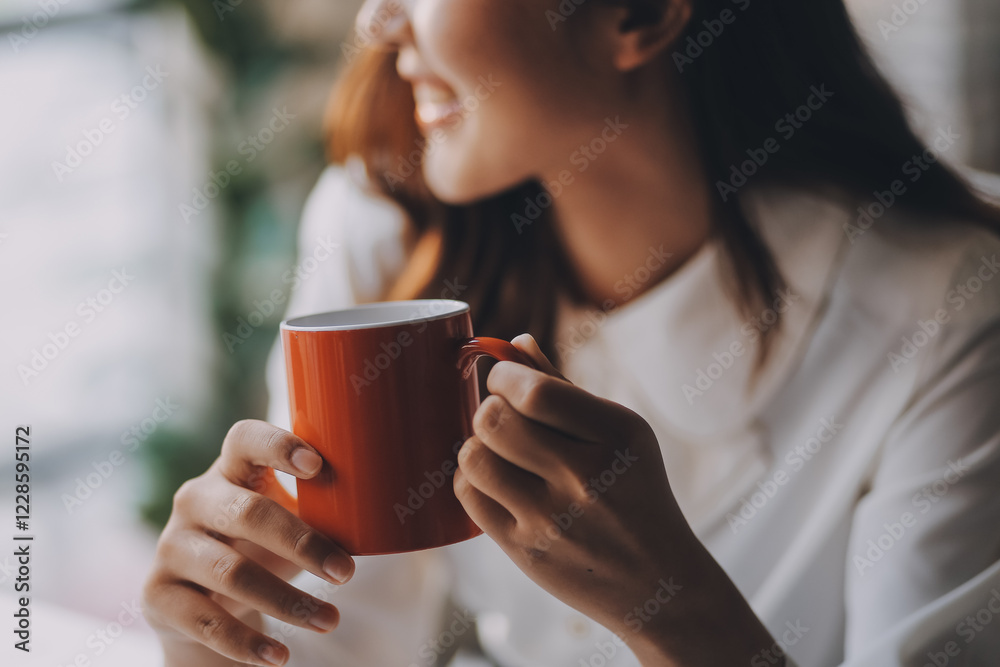 Young asian businesswoman sitting on an ergonomic chair and drinking coffee while working on a laptop computer in a modern office, she is smiling and looking at the screen Young asian businesswoman sitting on an ergonomic chair and drinking coffee while working on a laptop computer in a modern office, she is smiling and looking at the screen