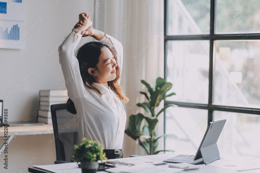 Office asian business woman stretching body for relaxing while working with laptop computer at her desk, office lifestyle, business situation Office asian business woman stretching body for relaxing while working with laptop computer at her desk, office lifestyle, business situation