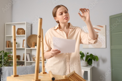Beautiful young thoughtful woman with manual and metal screw assembling wooden table at home
