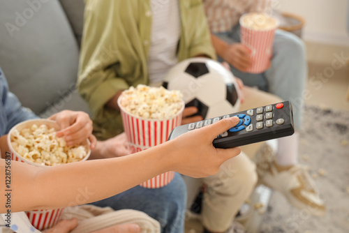 Happy family with TV remote control, popcorn and soccer ball watching football game at home, closeup