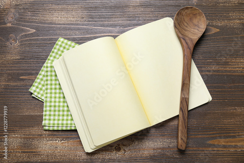 Blank recipe book, spoon and napkin on wooden background