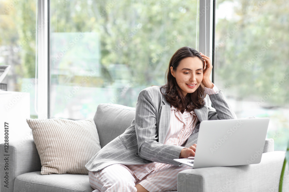 Young businesswoman working with laptop on sofa in office. National Wear Your Pajamas to Work Day Young businesswoman working with laptop on sofa in office. National Wear Your Pajamas to Work Day