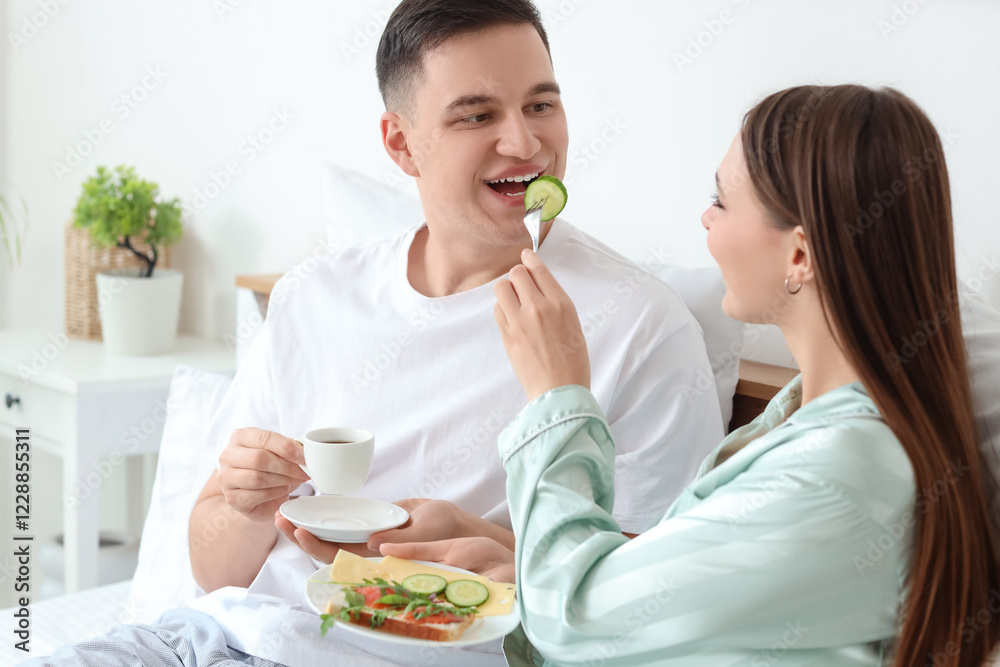 Young couple with coffee and sandwich having breakfast in bedroom Young couple with coffee and sandwich having breakfast in bedroom