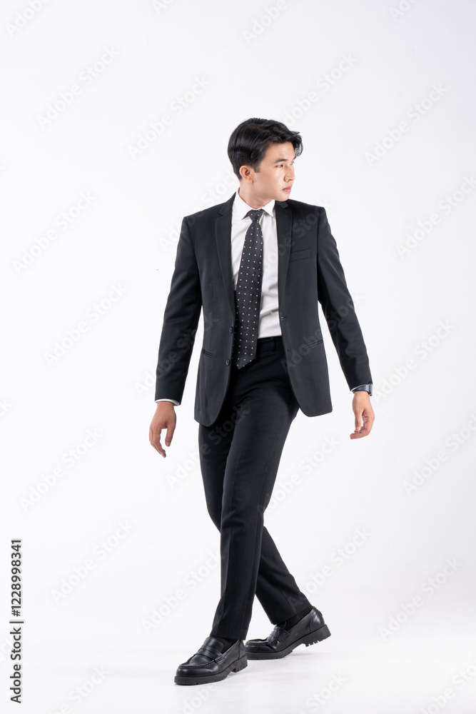 A man in a black suit and tie stands in front of a white background A man in a black suit and tie stands in front of a white background