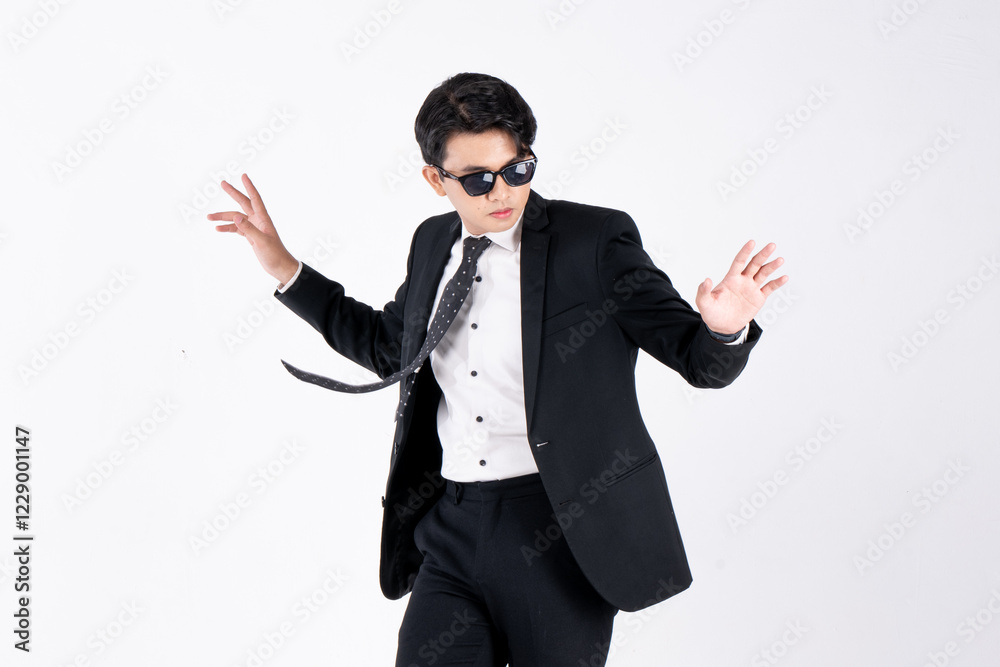 A man in a black suit and tie stands in front of a white background