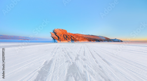 Car tire tracks (trail) in fresh snow - Ogoy island on winter Baikal lake with transparent cracked blue ice at sunrise - Baikal, Siberia, Russia photo