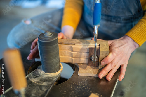 Unrecognizable carpenter hands turn, sand and polish wooden knife blanks on lathe machine. Woodworking detailed shaping, custom knife production, artisan skill, manual labor job, handcrafted tools photo