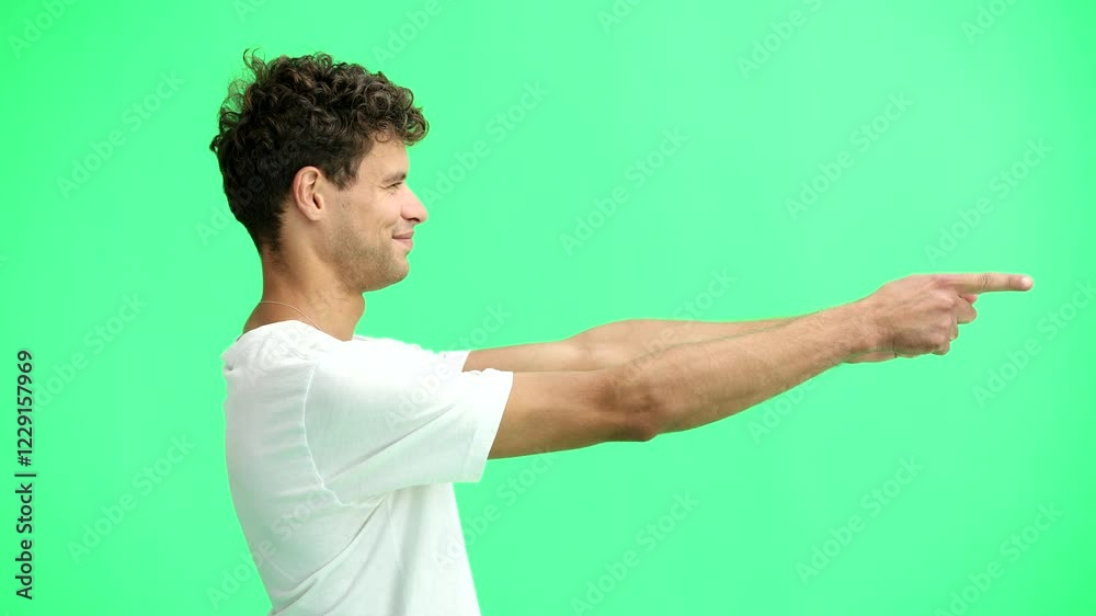A man in a white T-shirt, on a green background, close-up, pointing to the side A man in a white T-shirt, on a green background, close-up, pointing to the side