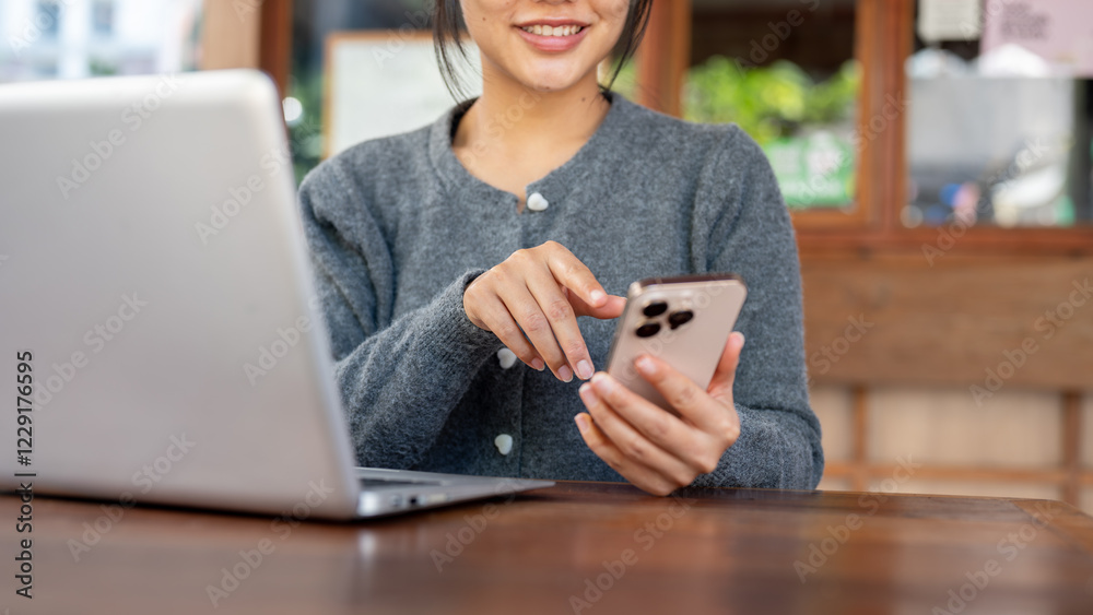 A happy Asian woman responds to messages on her smartphone while working remotely from a coffee shop A happy Asian woman responds to messages on her smartphone while working remotely from a coffee shop