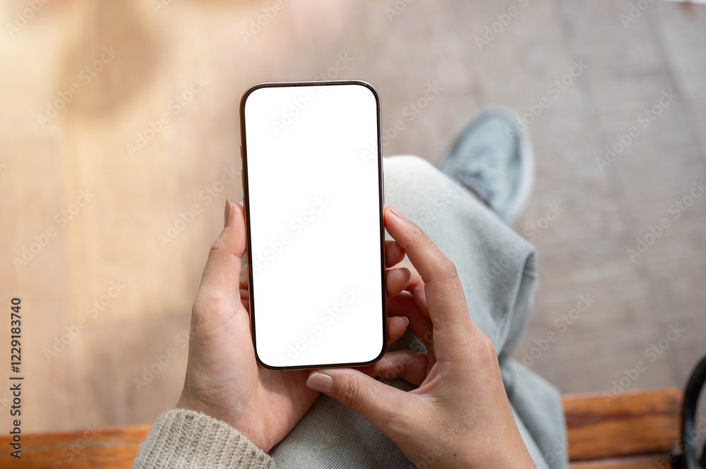 © bongkarn - A top view of a woman sits indoors and holds a smartphone with a white screen mockup.