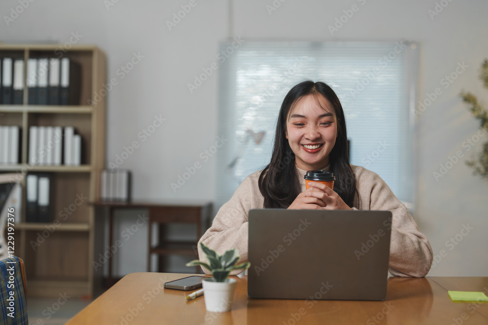 Young asian businesswoman working remotely in a cozy home office, smiling while enjoying a hot beverage and engaging with her laptop, radiating positivity and comfort Young asian businesswoman working remotely in a cozy home office, smiling while enjoying a hot beverage and engaging with her laptop, radiating positivity and comfort